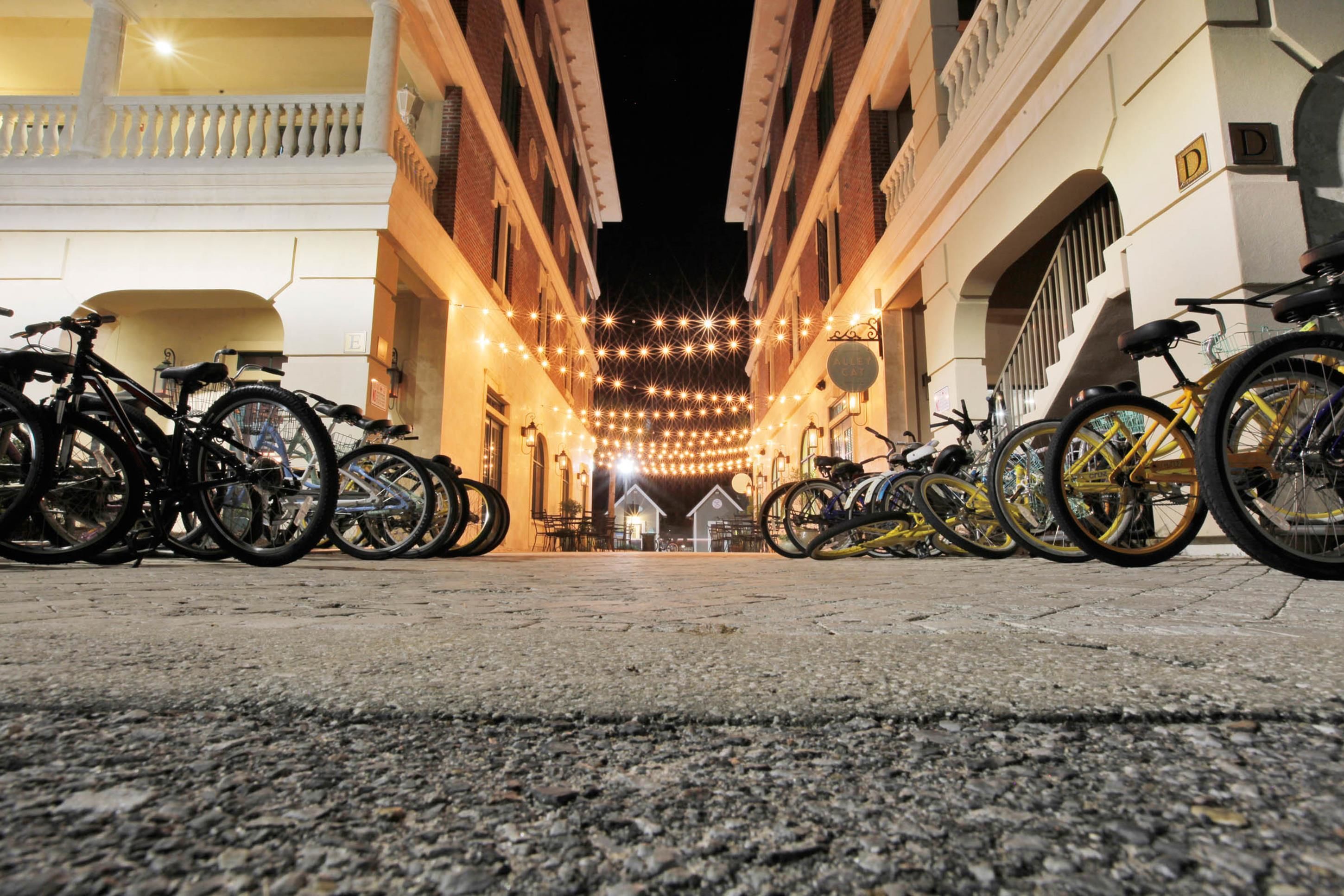 A nighttime view of a narrow street lined with bicycles and buildings, featuring a string of lights overhead.