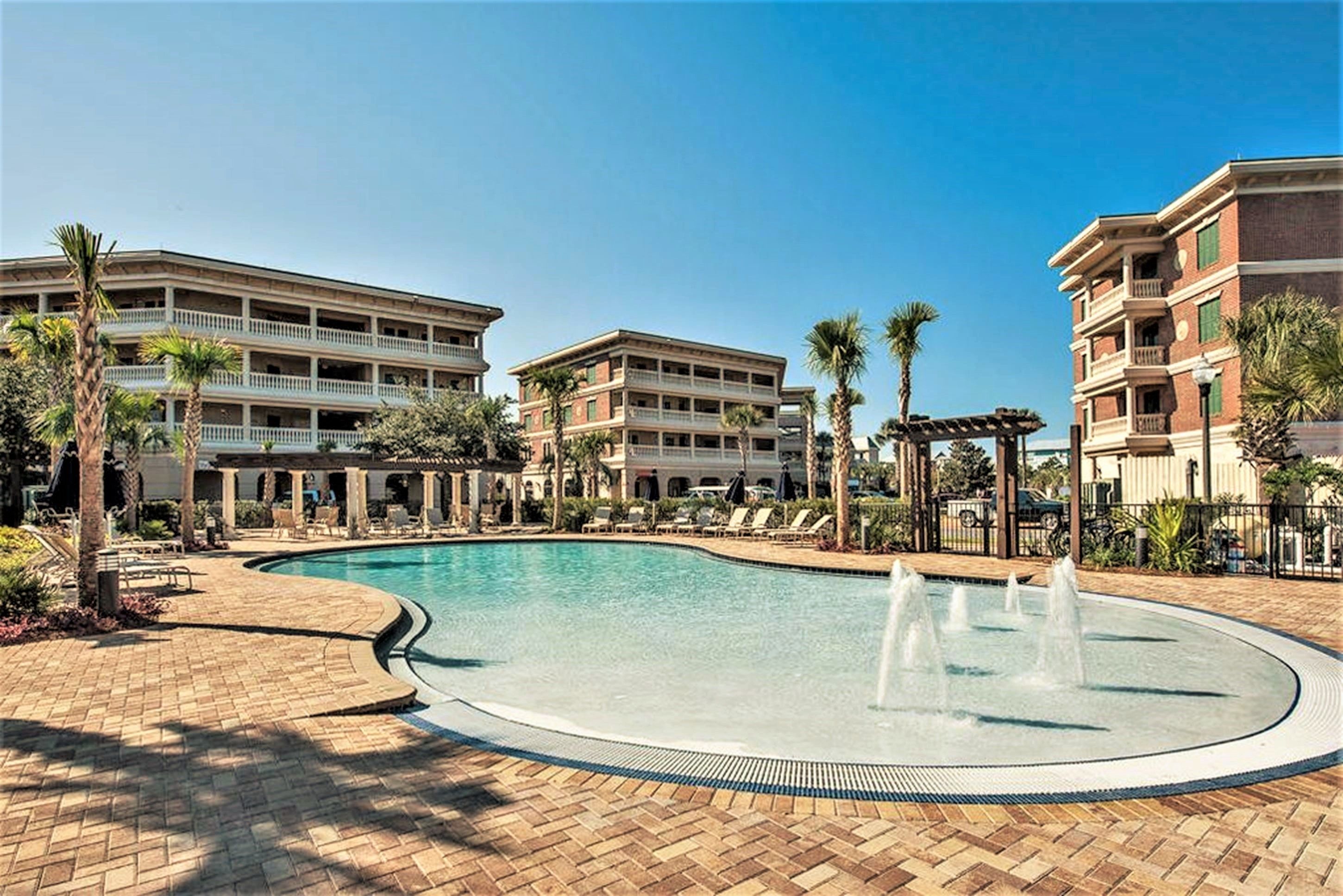 A hotel with a swimming pool, palm trees, and a covered area with lounge chairs.