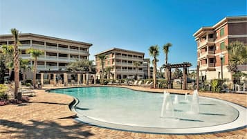 A hotel with a swimming pool, palm trees, and a covered area with lounge chairs.