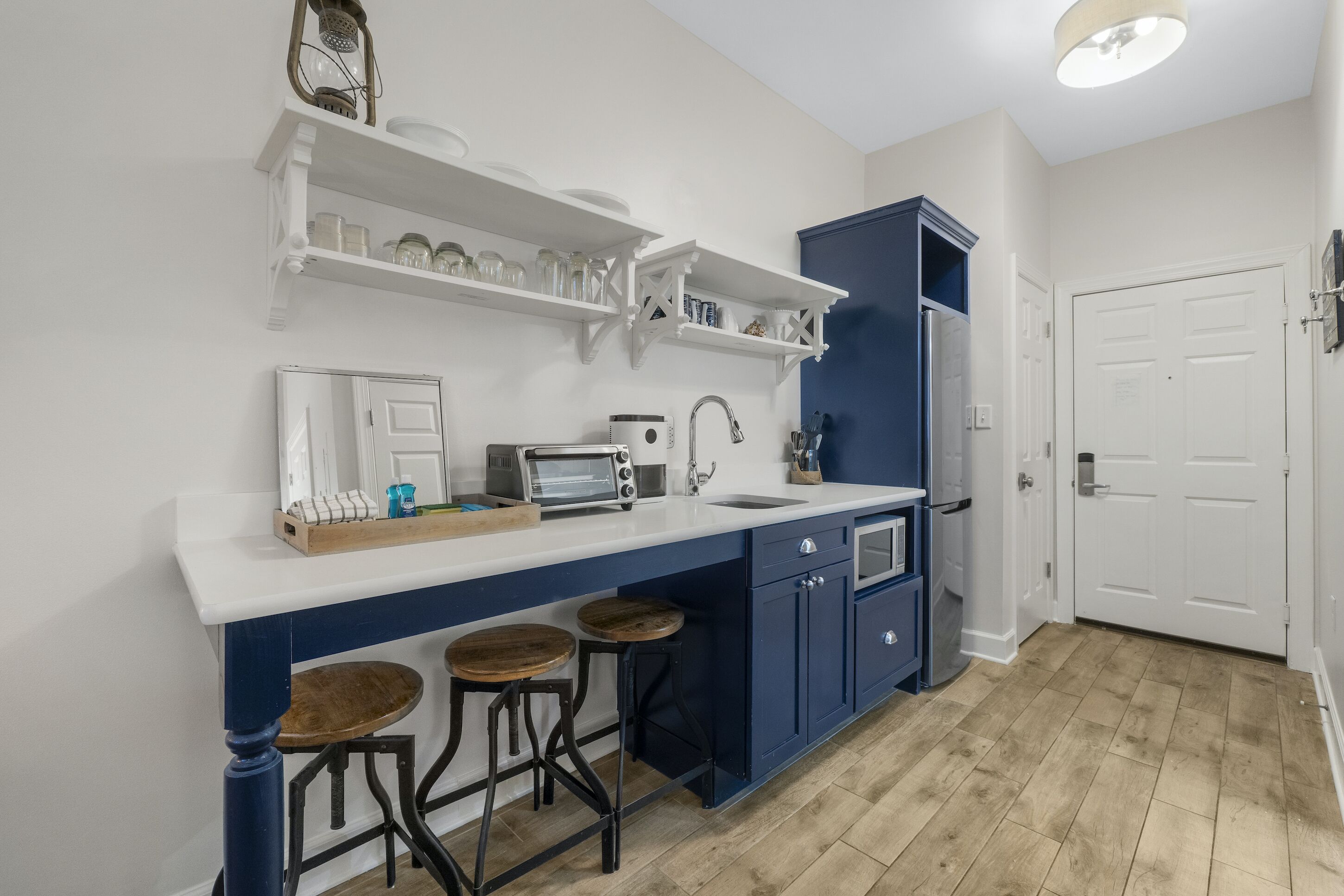 Une cuisine avec un plan de travail blanc, des placards bleus et un plancher en bois.