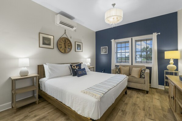 A bedroom with a large bed, a nightstand, a dresser, a window with blinds, and a chandelier.