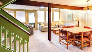 Una sala de estar acogedora con una escalera de madera, una mesa de comedor y un conjunto de sofás.
