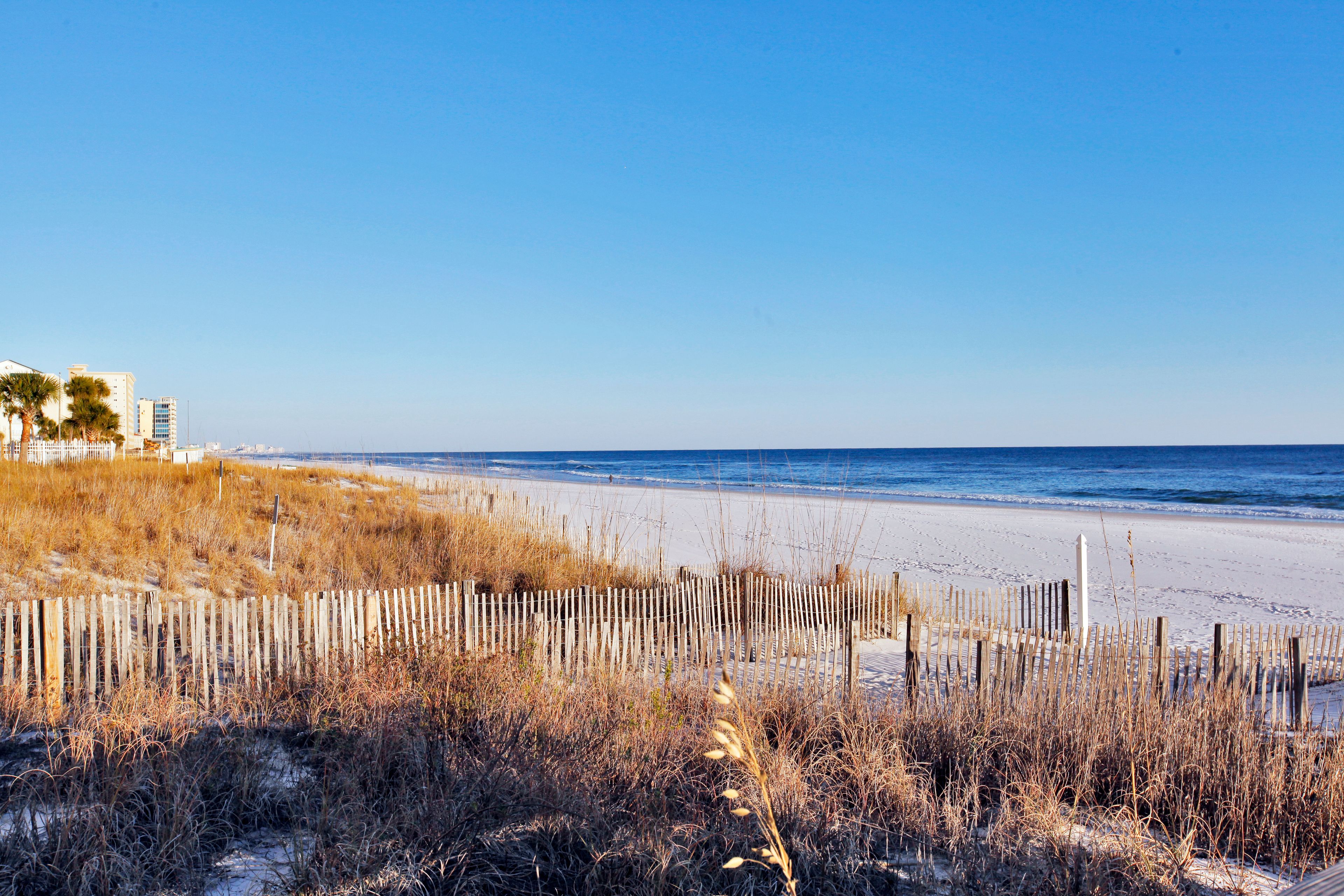 A beach with a wooden fence, sandy shore, and buildings in the background.