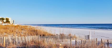 A beach with a wooden fence, sandy shore, and buildings in the background.
