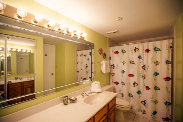 Un baño con tocador, lavabo, espejo y cortina de ducha con estampado de peces.