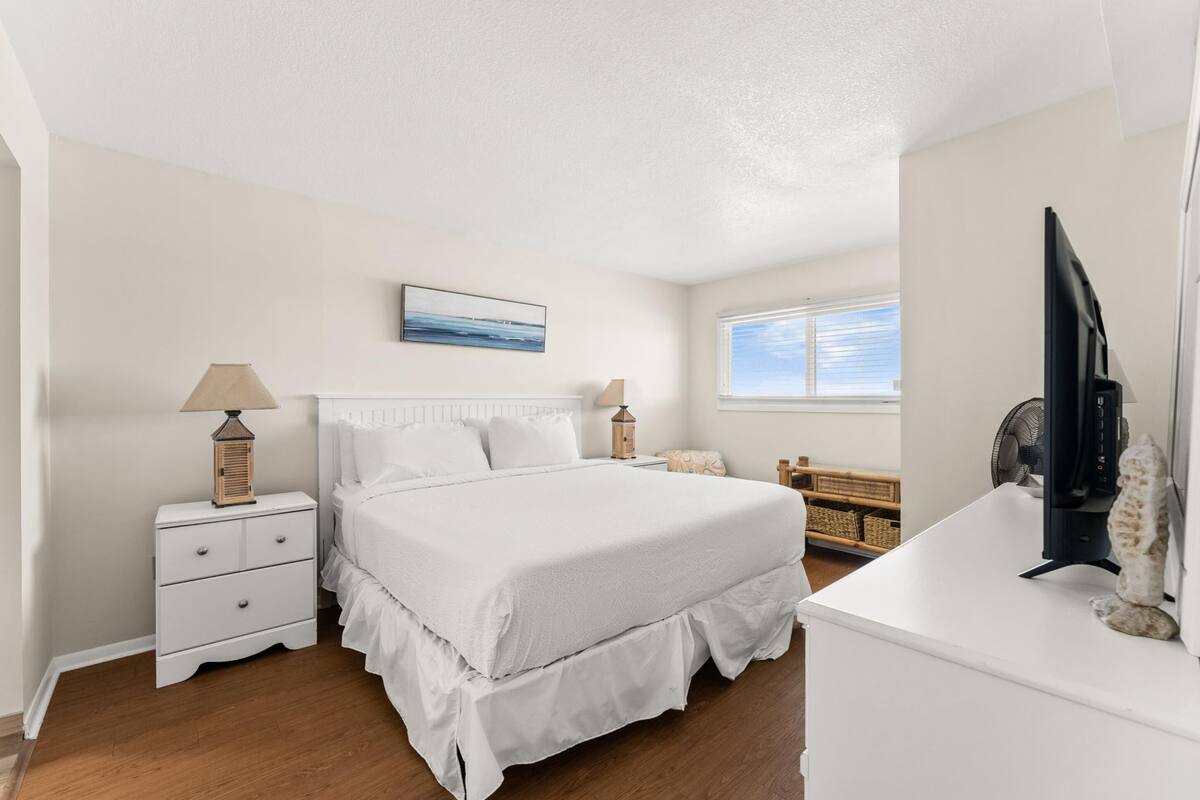 A bedroom with a bed, bedside tables, a lamp, a TV, and a window.