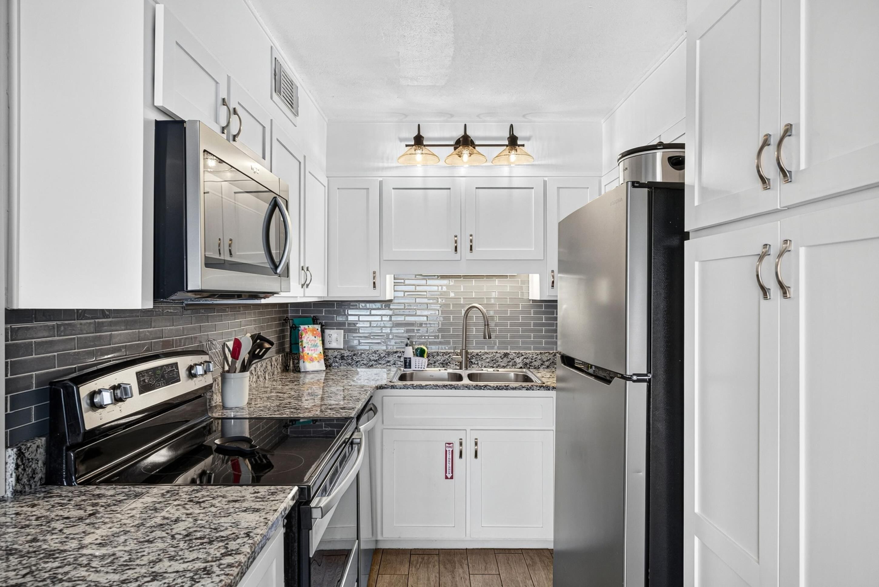 Cocina moderna con armarios blancos, encimera de granito, refrigerador de acero inoxidable y horno empotrado.