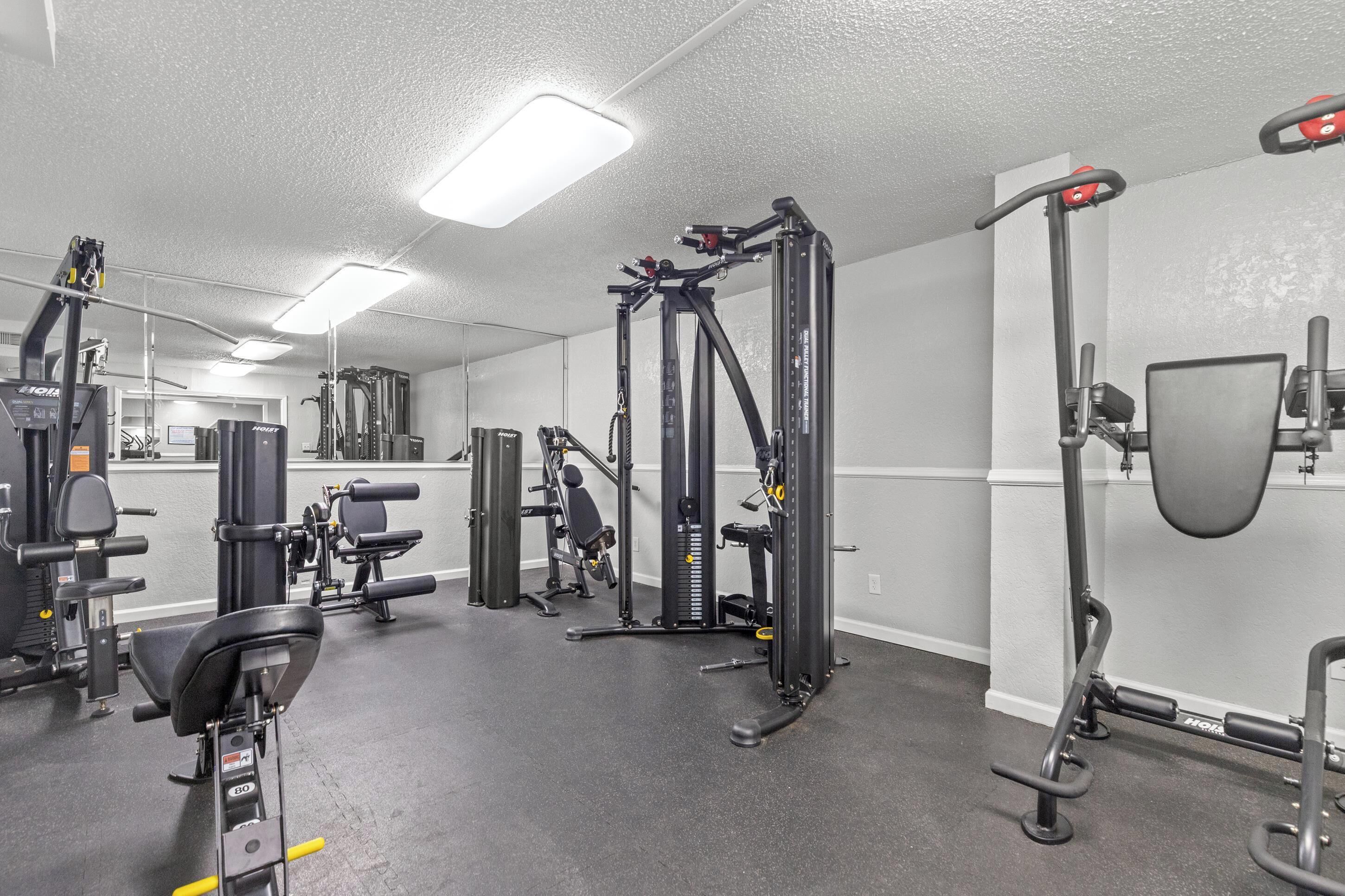 A gym with various exercise equipment, including a bench press, squat rack, and cable machine.