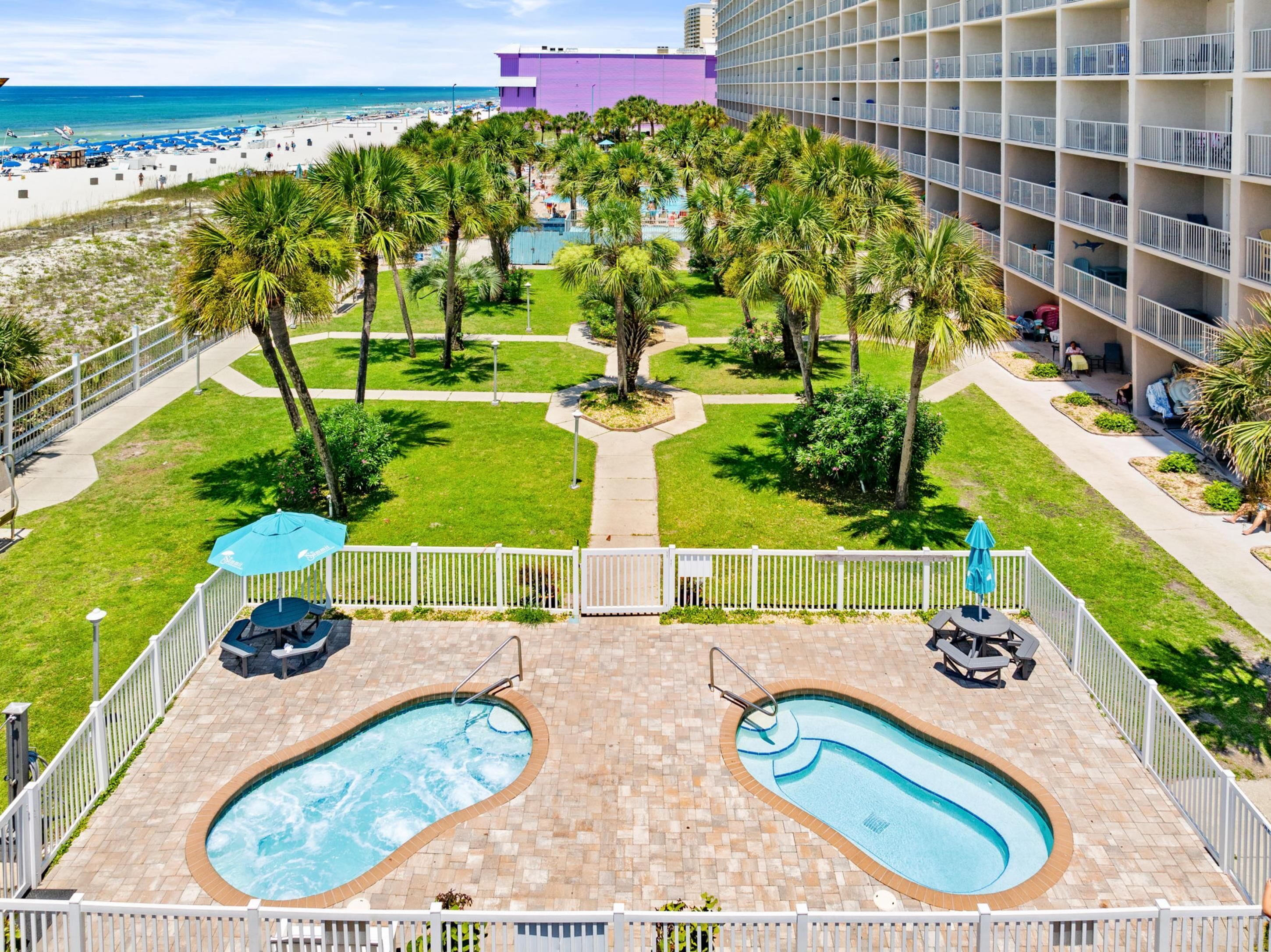 A hotel pool area with two pools, palm trees, and a beach view.