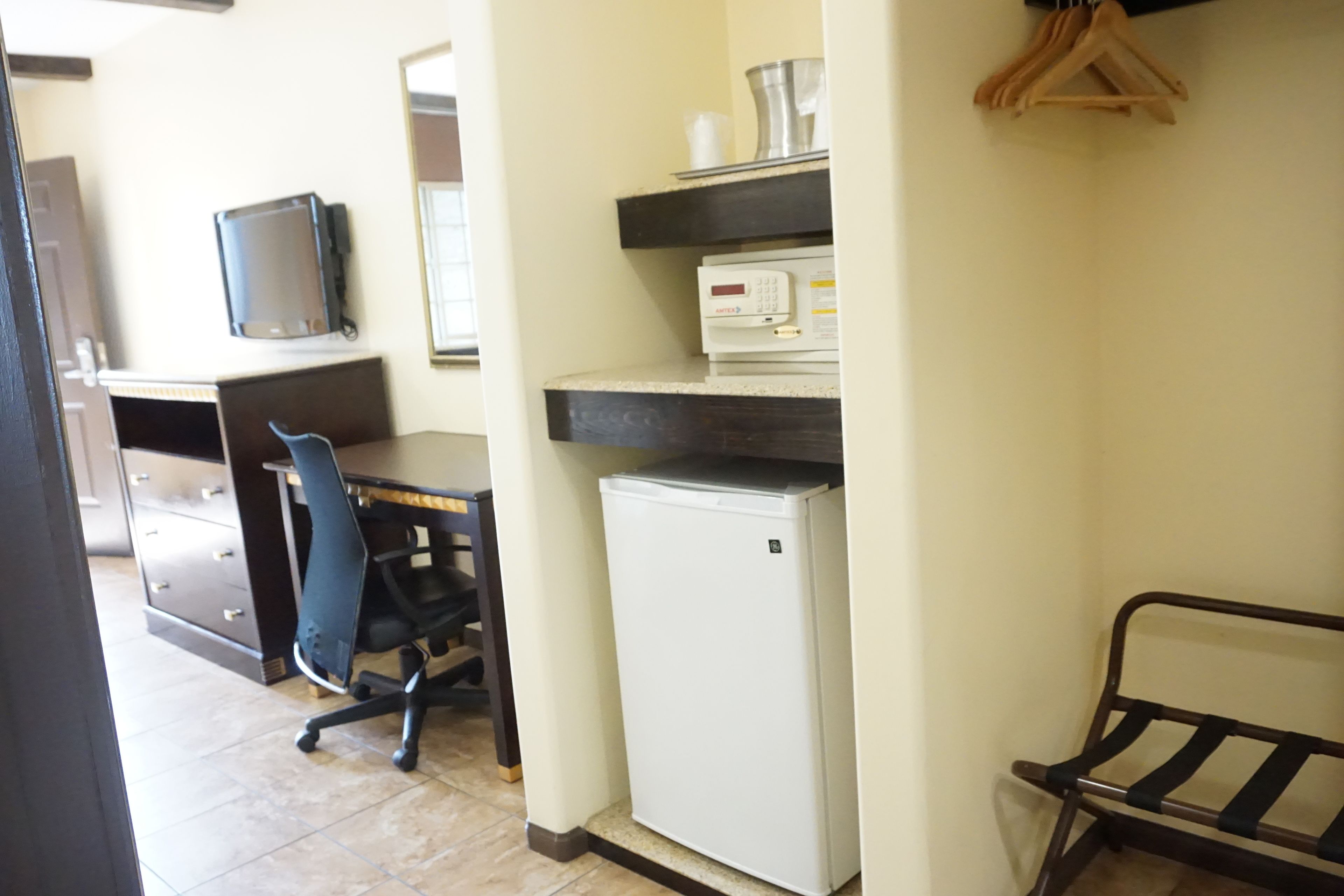 Un petit bureau avec un bureau, une chaise, un réfrigérateur et un téléviseur posé sur une étagère.