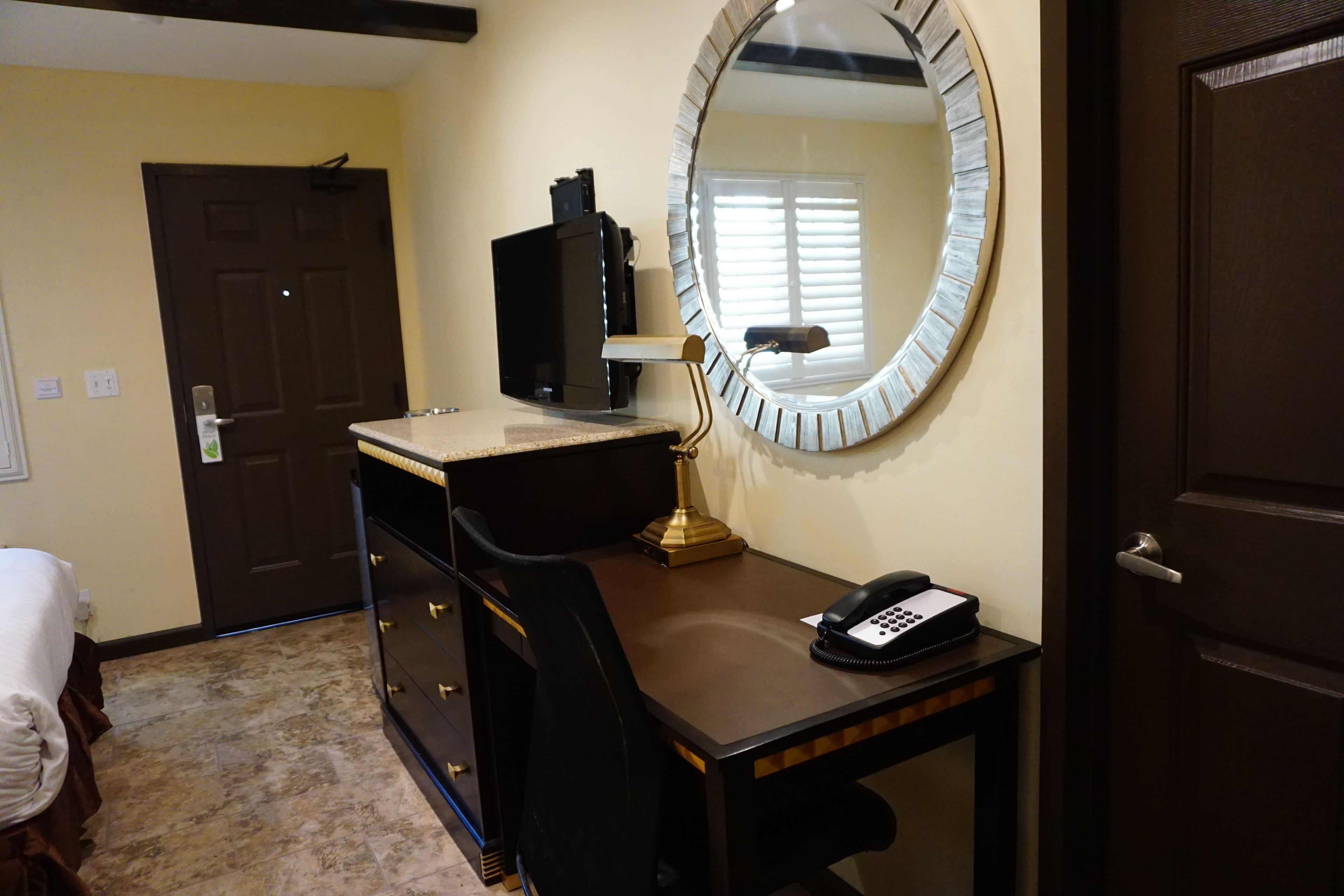 A hotel room with a desk, a mirror, a telephone, and a bed.