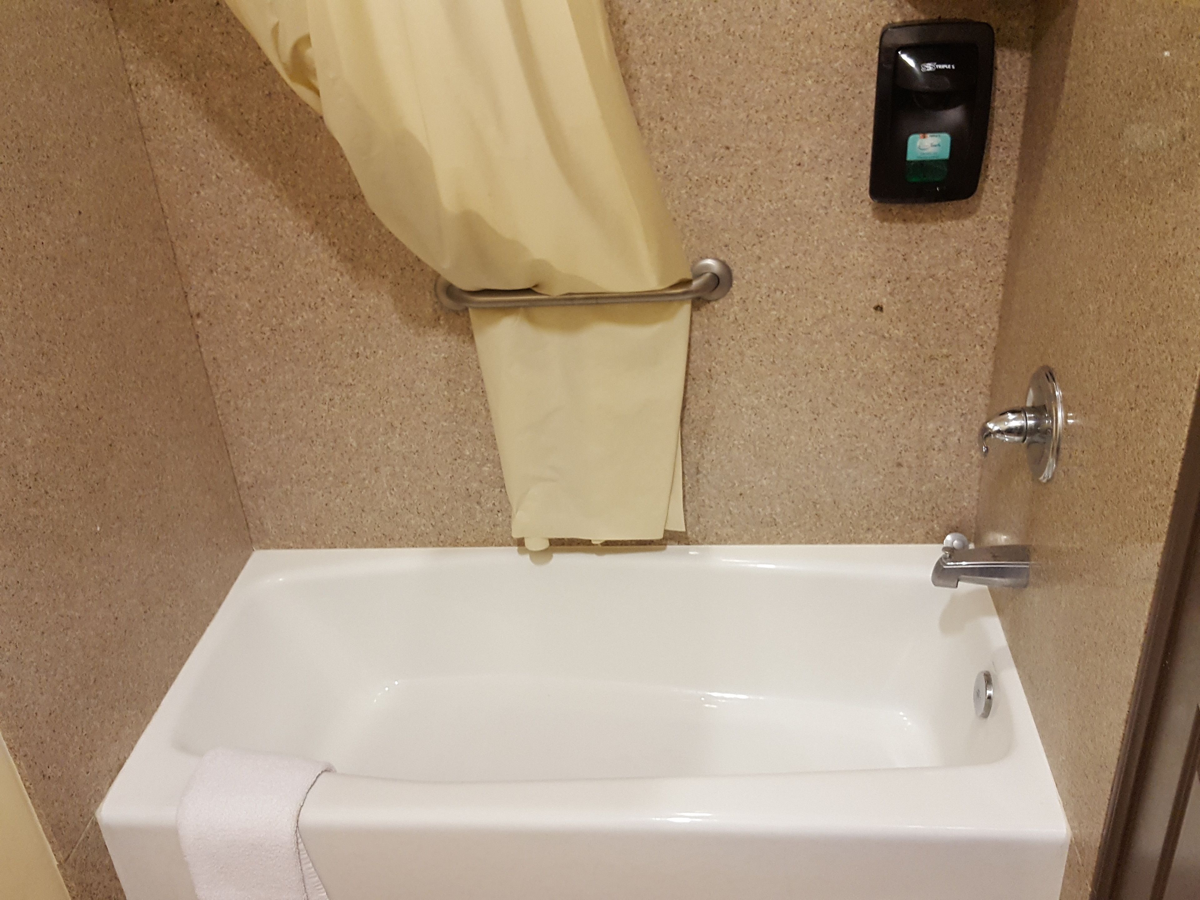 Une baignoire blanche, une serviette, un rideau de douche et un distributeur de savon fixé au mur.