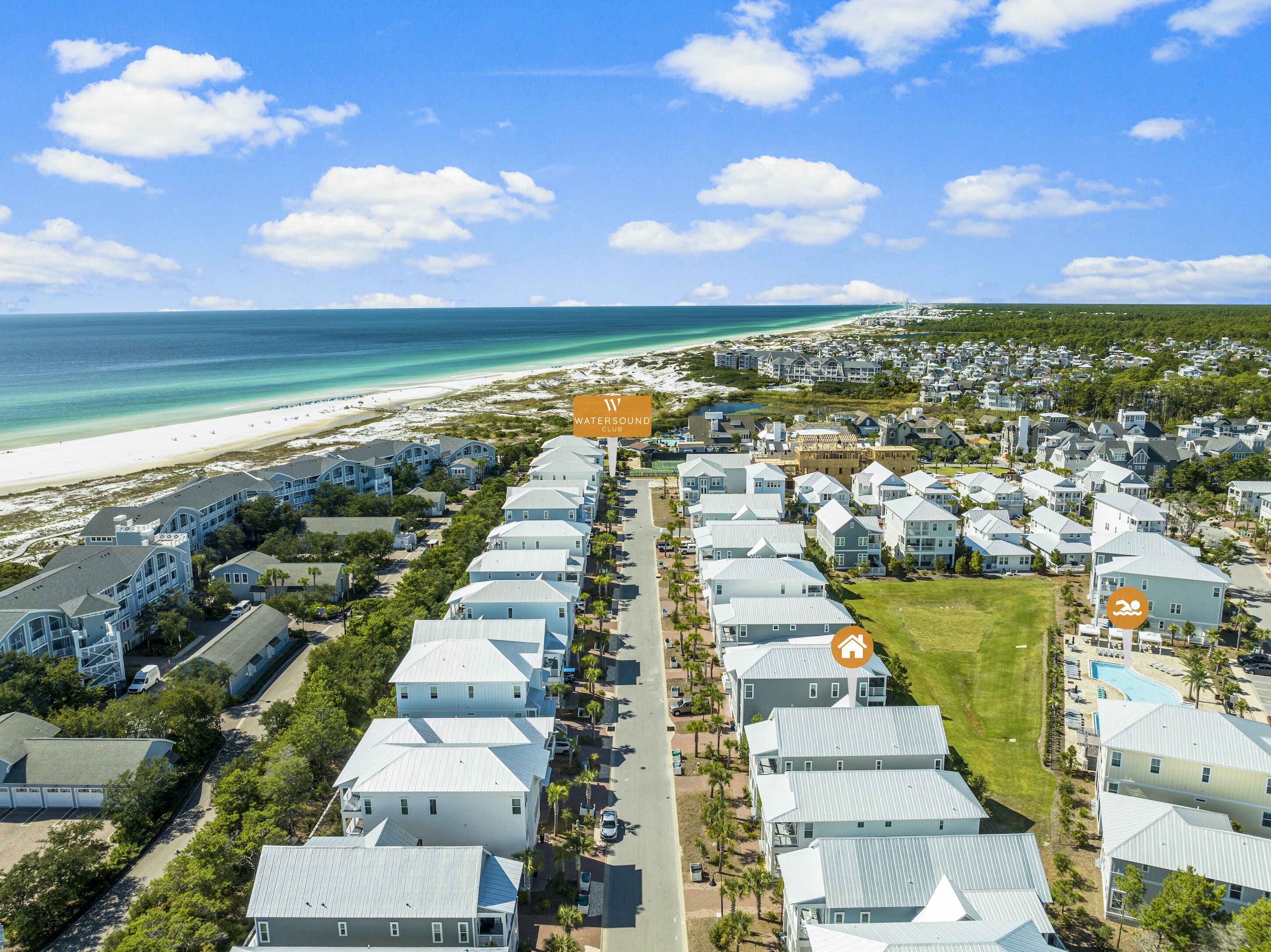 An aerial view of a coastal residential area with houses, a beach, and a swimming pool.
