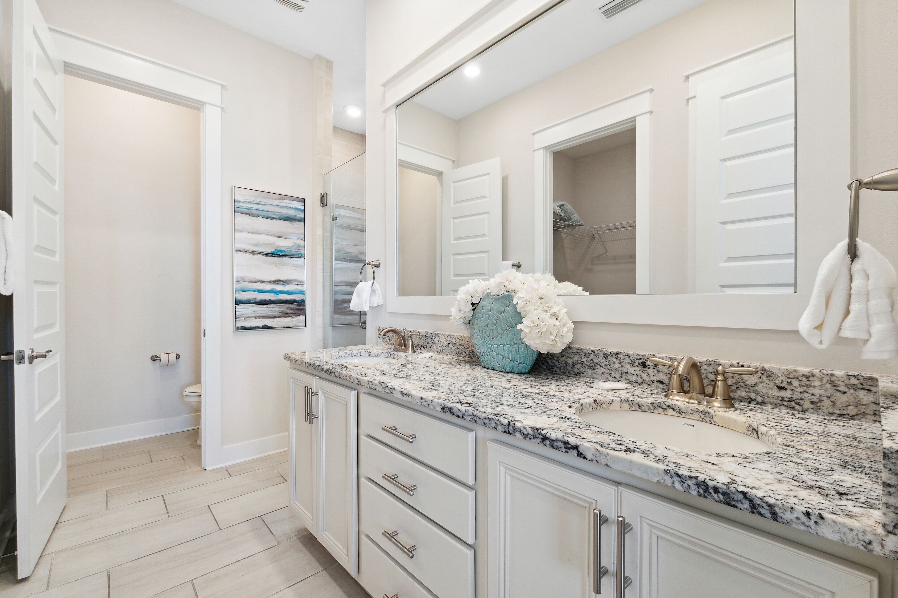 Une salle de bain moderne avec un grand miroir, un comptoir en granit et un lavabo doté de robinetterie dorée.