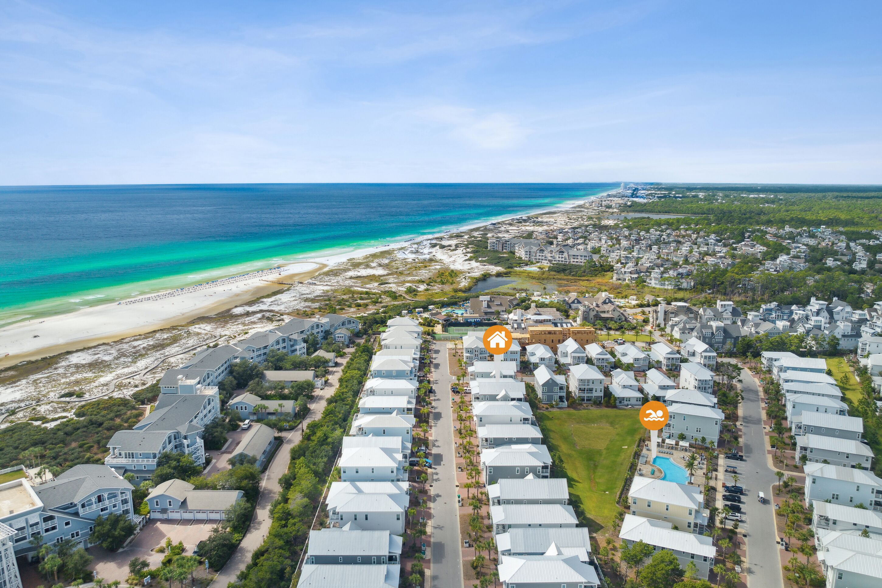 An aerial view of a coastal resort with beachfront properties, a central road, and a swimming pool area.