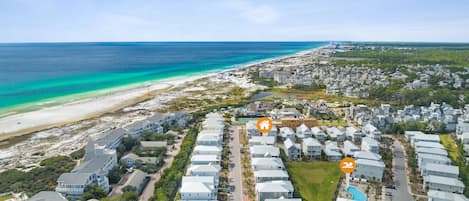 An aerial view of a coastal resort with beachfront properties, a central road, and a swimming pool area.