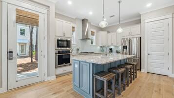 A modern kitchen with white cabinets, a large island with bar stools, stainless steel appliances, and a view through the glass door.