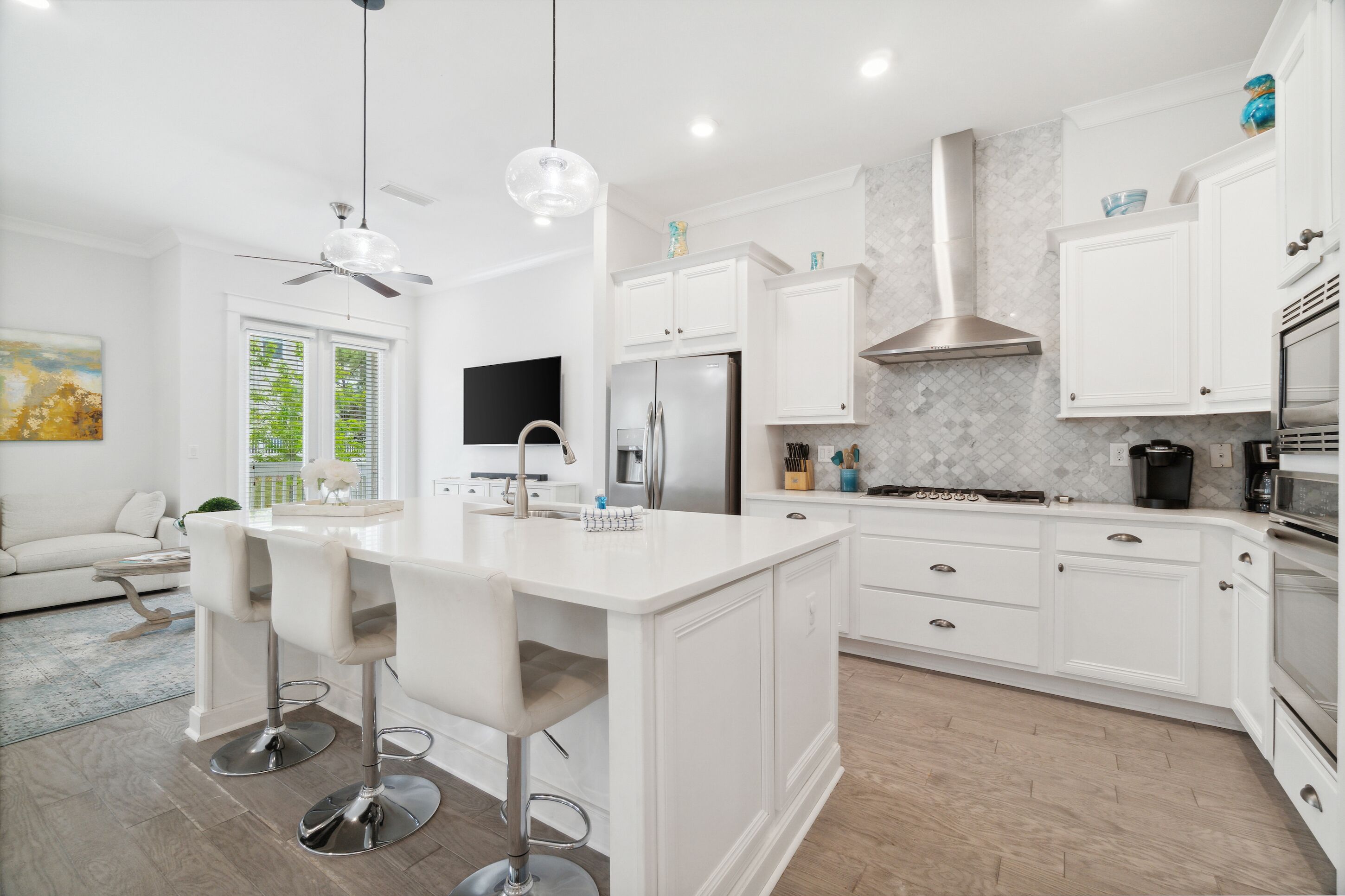 A modern kitchen with white cabinetry, a central island with bar stools, a stainless steel refrigerator, and a built-in oven.