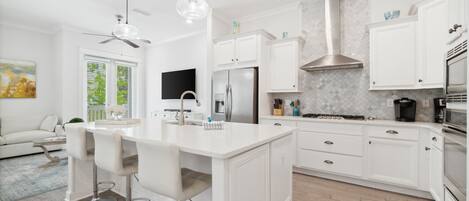 A modern kitchen with white cabinetry, a central island with bar stools, a stainless steel refrigerator, and a built-in oven.