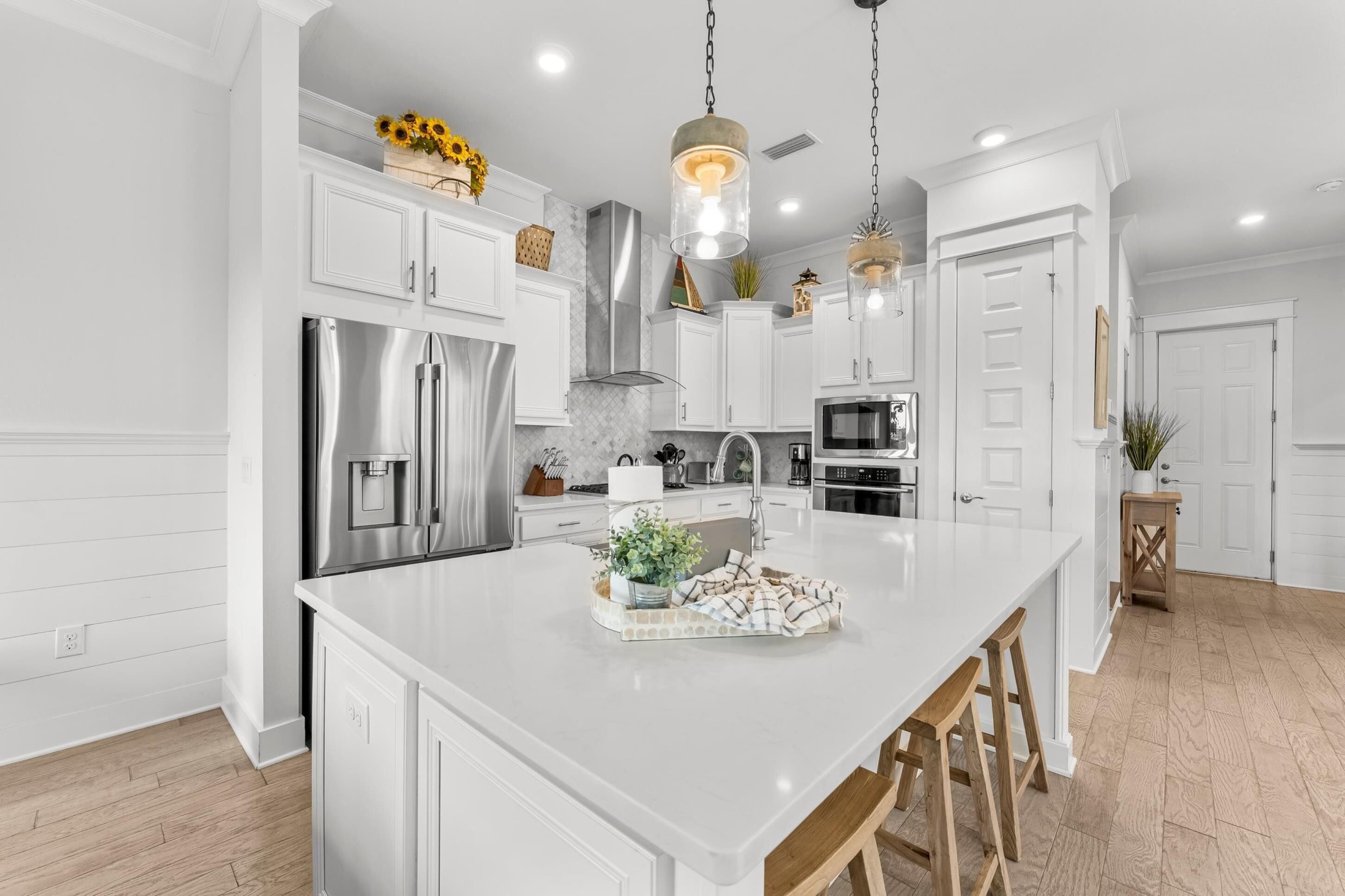 A modern kitchen with white cabinetry, stainless steel appliances, and a central island with stools.