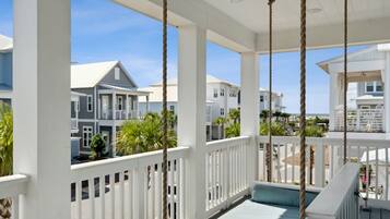 A covered porch with white railings, a ceiling fan, and a view of neighboring houses and palm trees.