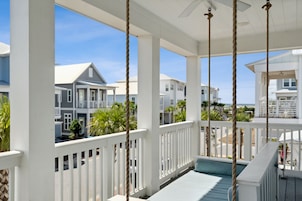 A covered porch with white railings, a ceiling fan, and a view of neighboring houses and palm trees.