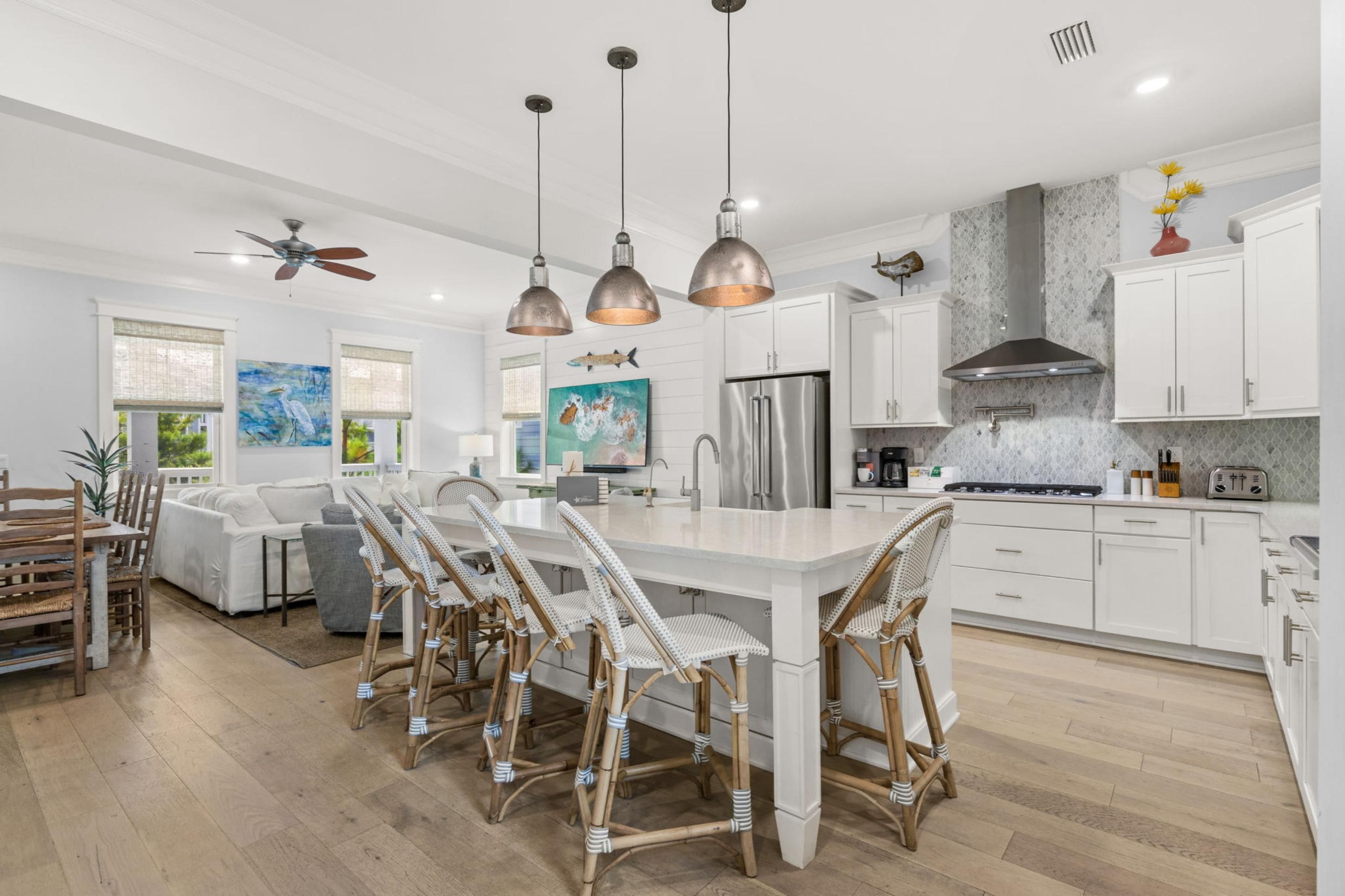 A modern kitchen with a central island, white cabinetry, and a dining area with wicker chairs.