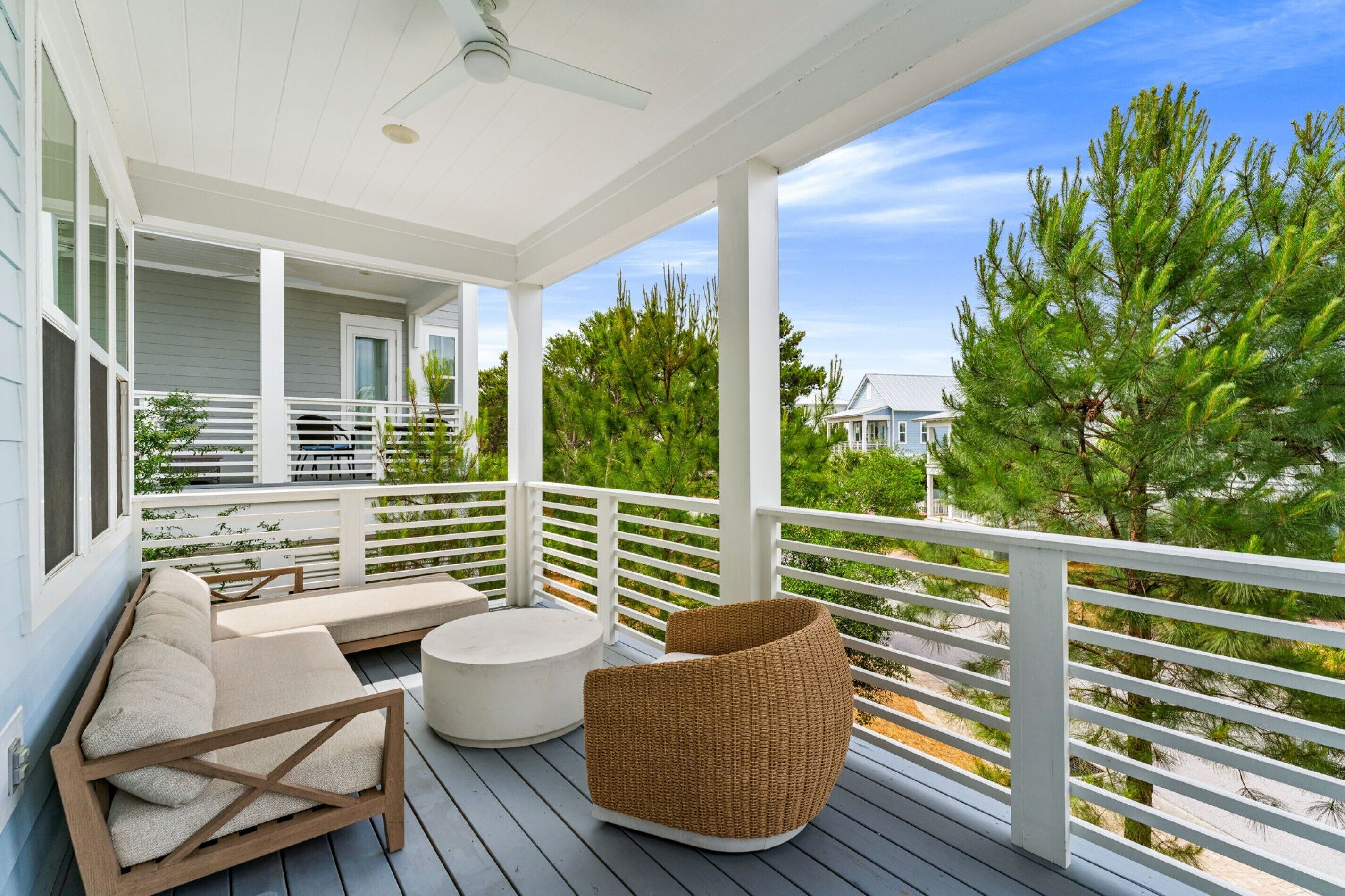 A covered porch with a sofa, a round table, and a wicker chair.