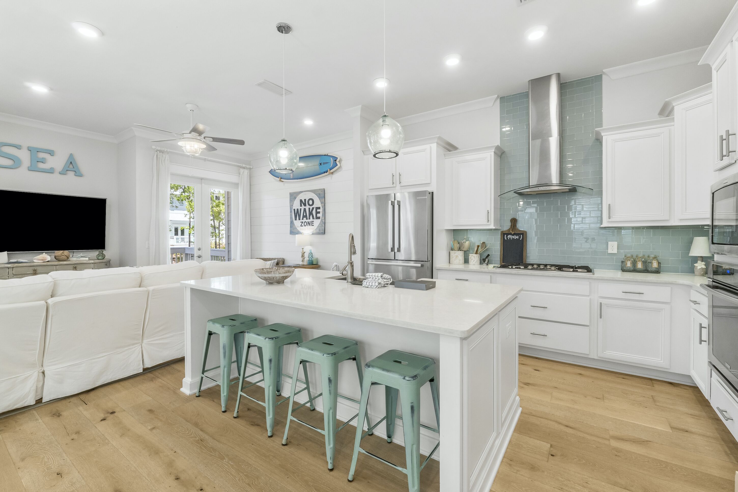 Une cuisine moderne avec des meubles blancs, un grand îlot central doté de tabourets, des appareils en acier inoxydable et un ventilateur de plafond.