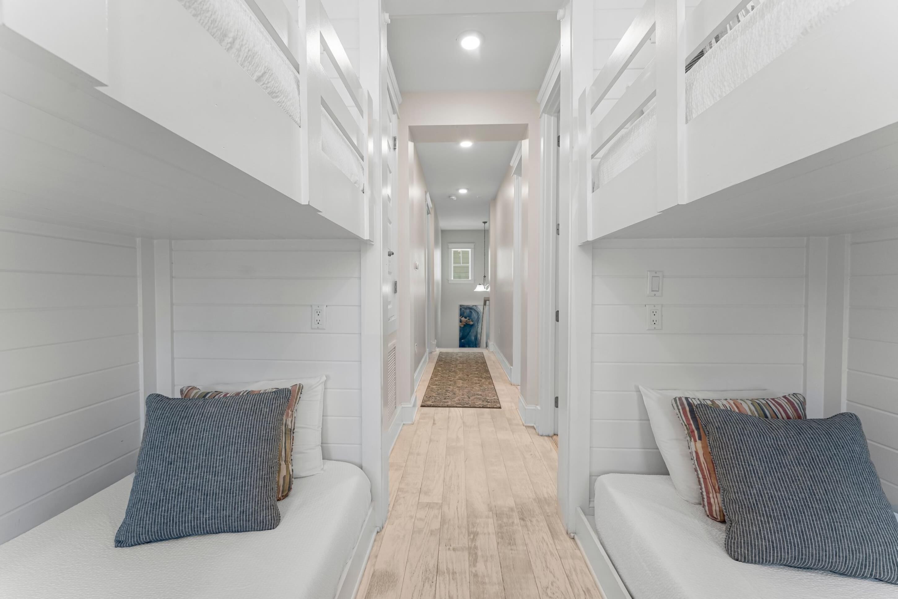Un couloir étroit avec deux lits de chaque côté, un plancher en bois et une vue sur une pièce au fond.