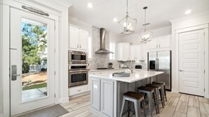 Una cocina moderna con armarios blancos, electrodomésticos de acero inoxidable, una isla central con taburetes y vistas al exterior.