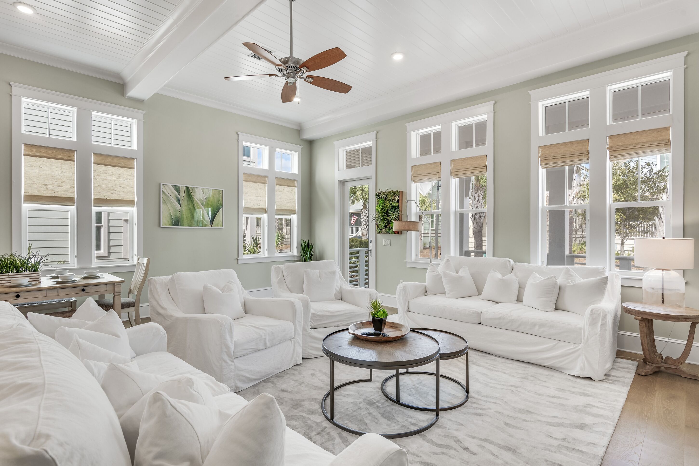 A spacious living room with white furniture, large windows, and a ceiling fan.