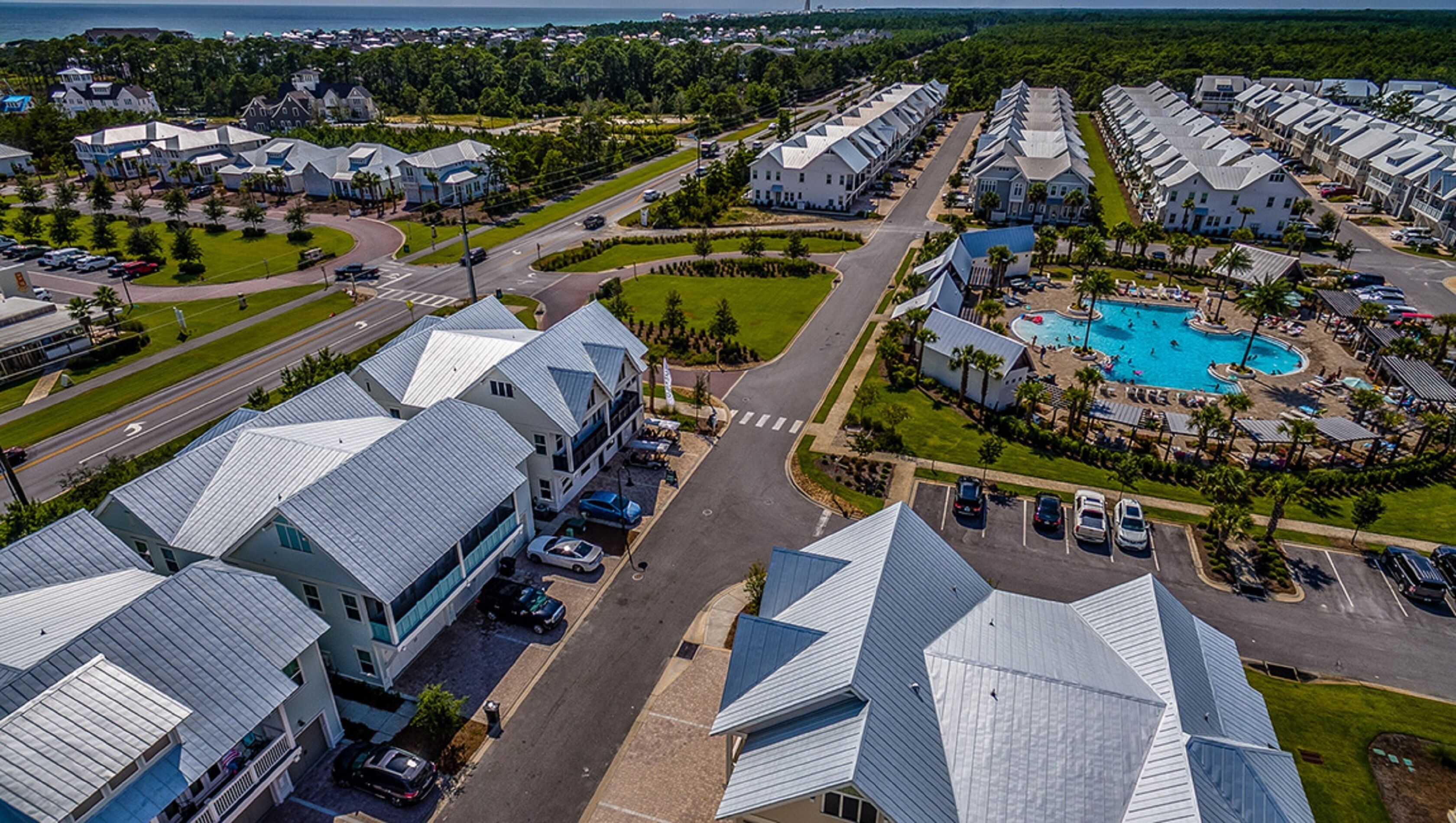 A residential area with modern houses, a central road, and a swimming pool with lounge areas.
