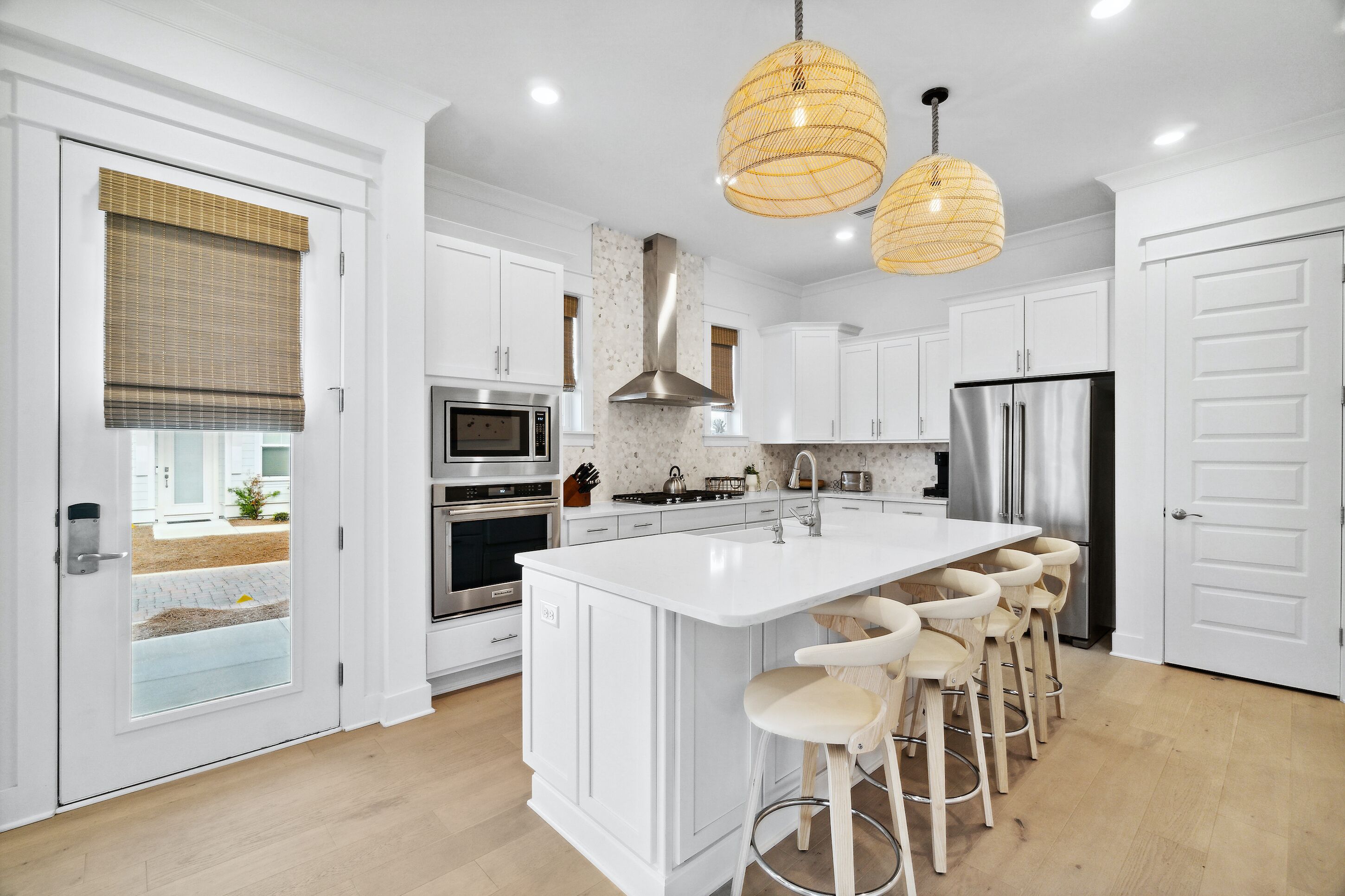 Una cocina moderna con armarios blancos, una isla grande con taburetes de bar, electrodomésticos de acero inoxidable y dos lámparas colgantes.