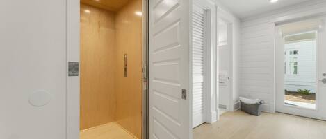 A modern interior with a wooden elevator, white doors, and a view of a house through a glass door.