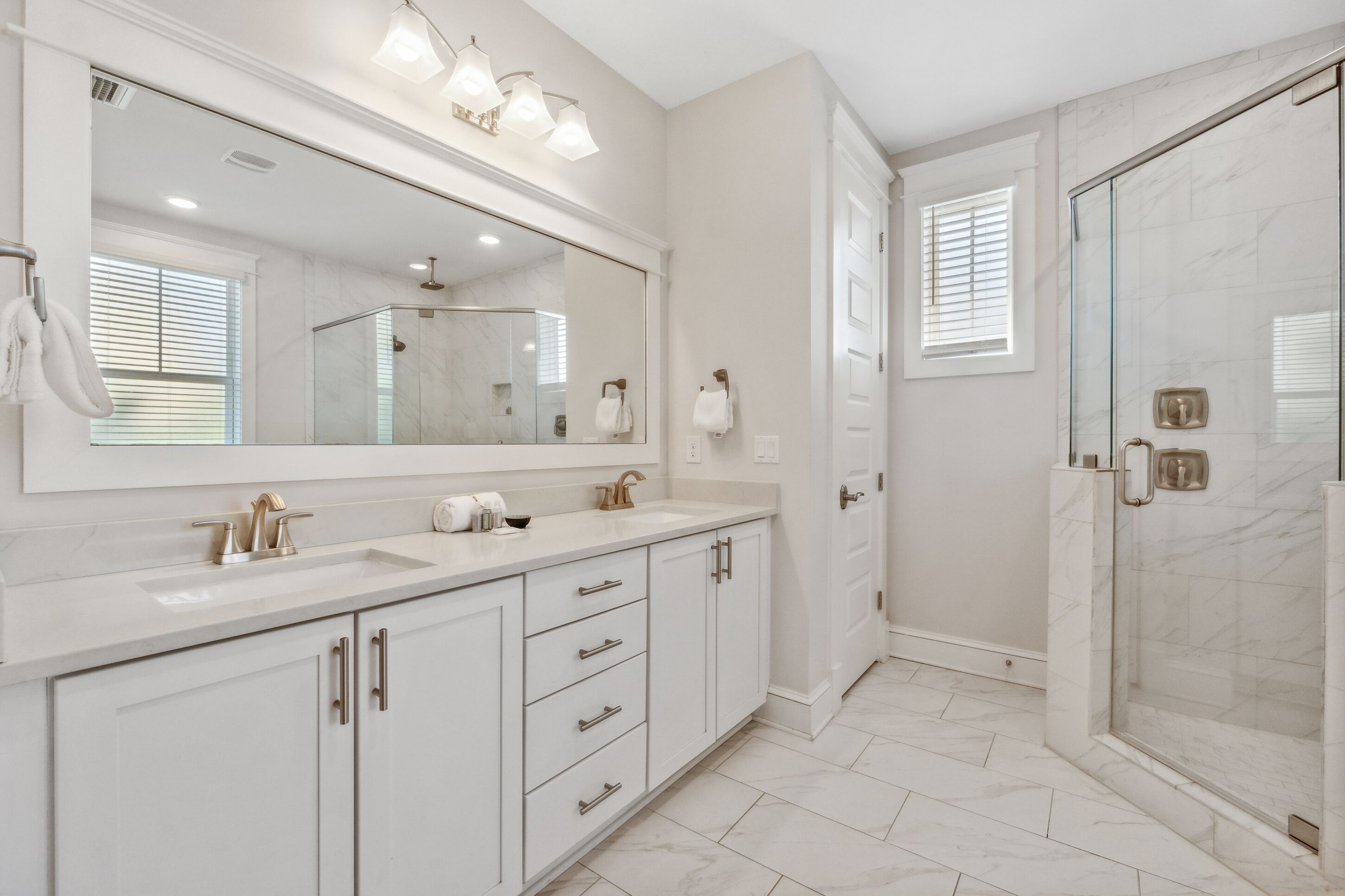 Un baño moderno con un espejo grande, dos lavamanos, una ducha y zona de ducha con paredes de vidrio.
