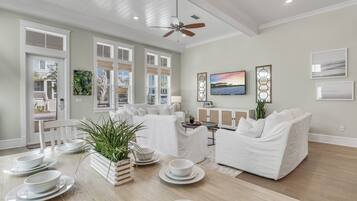 A spacious living room with a white sofa, a dining table set with plates and bowls, and a ceiling fan.