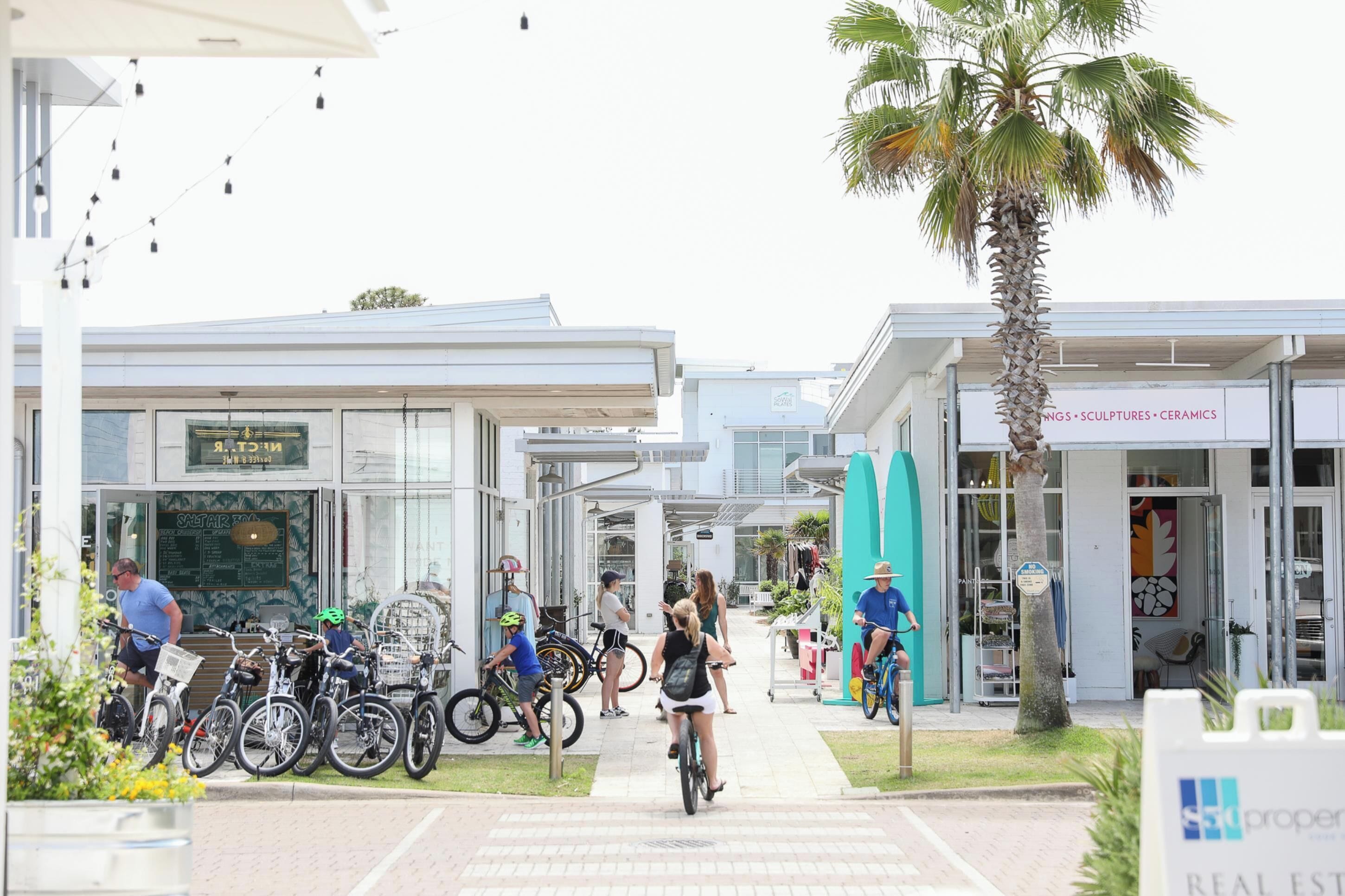Un edificio moderno con escaparates de vidrio, zona de estacionamiento para bicicletas y una palmera.