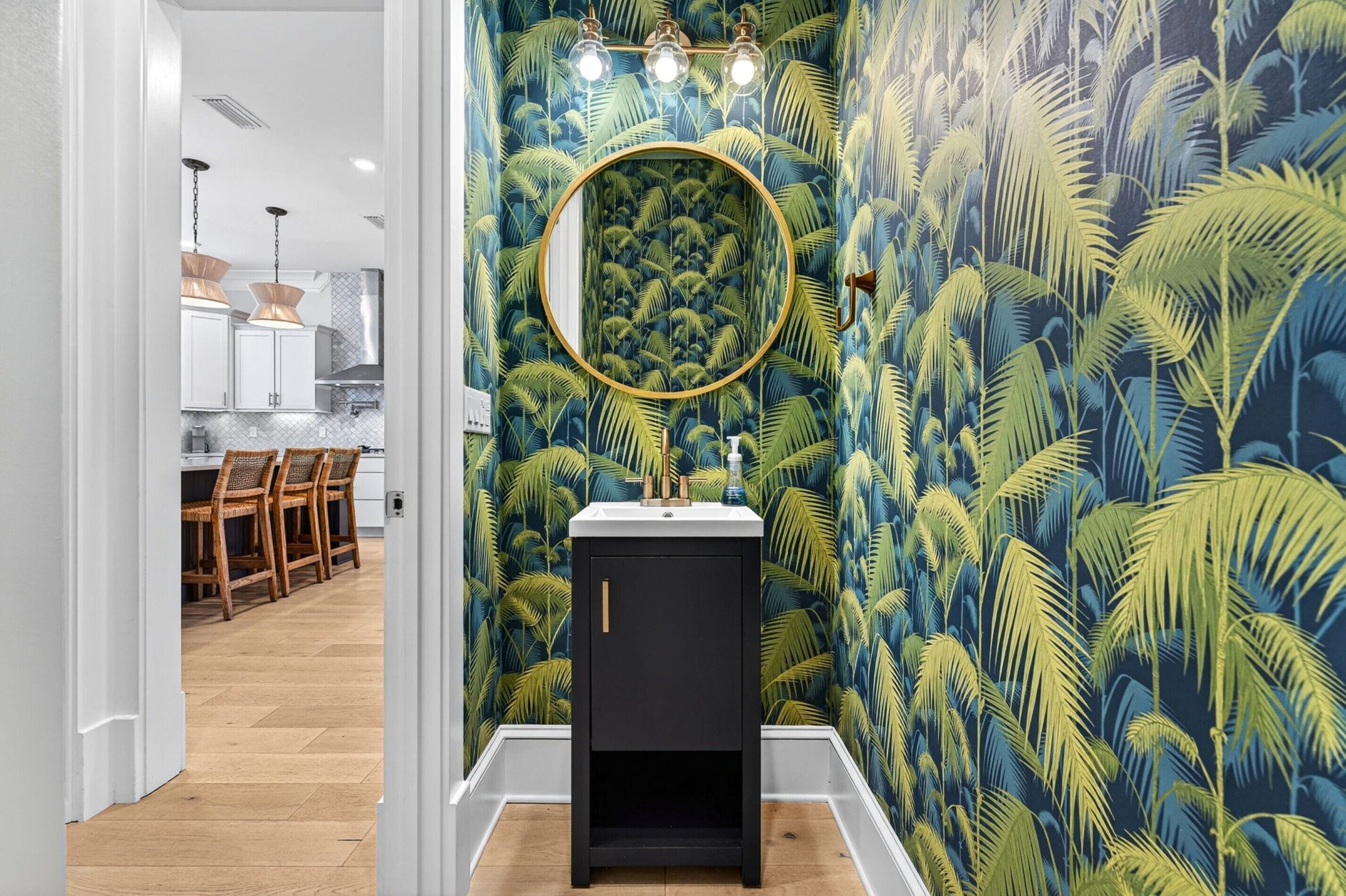 Une salle de bain avec un miroir rond, un lavabo et un mur orné d’un motif de feuilles tropicales.
