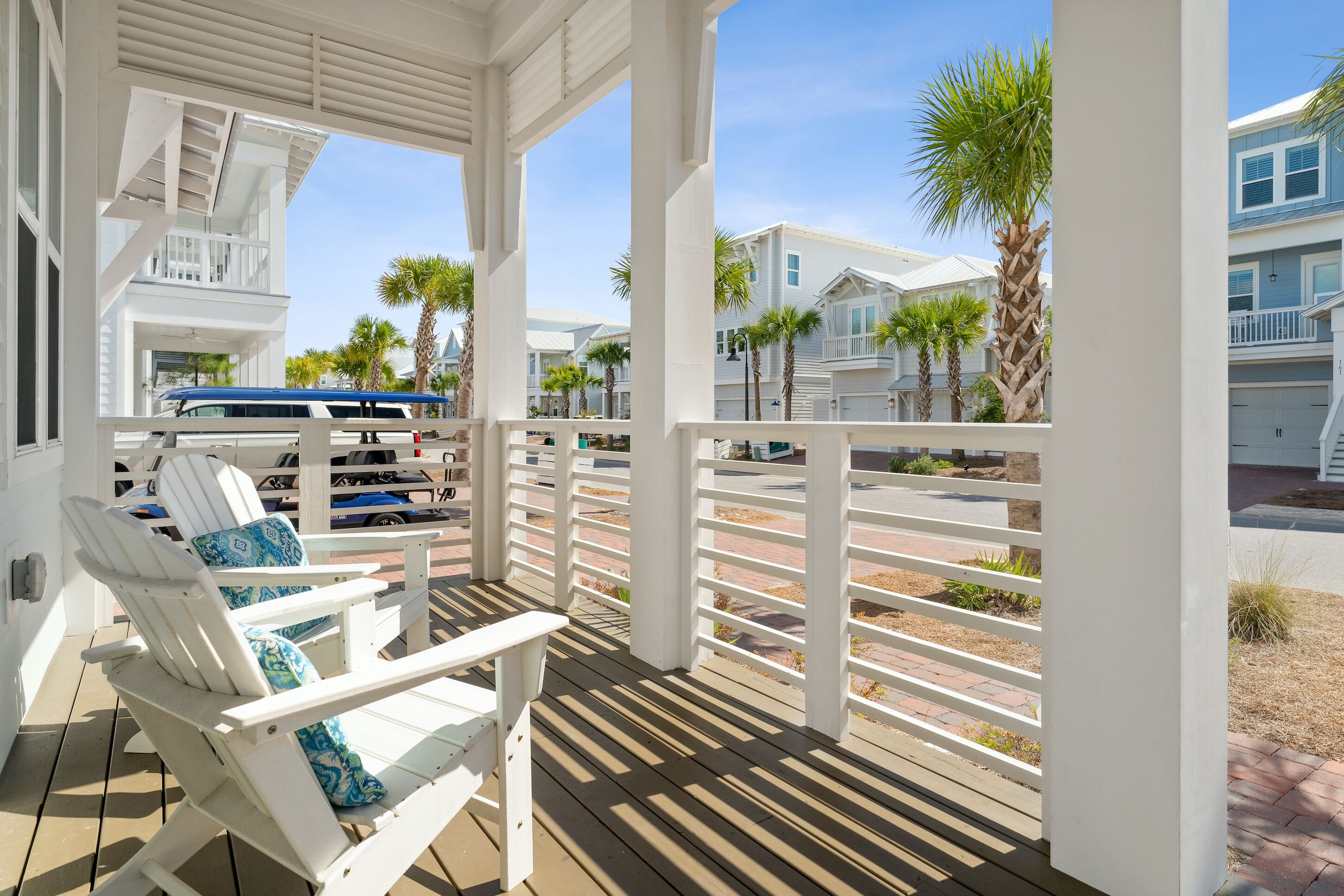 A covered outdoor area with white railings, a wooden deck, and a row of beach houses in the background.
