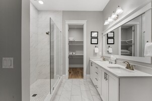 Un baño moderno con ducha a ras de suelo, tocador con un espejo grande y vestidor.
