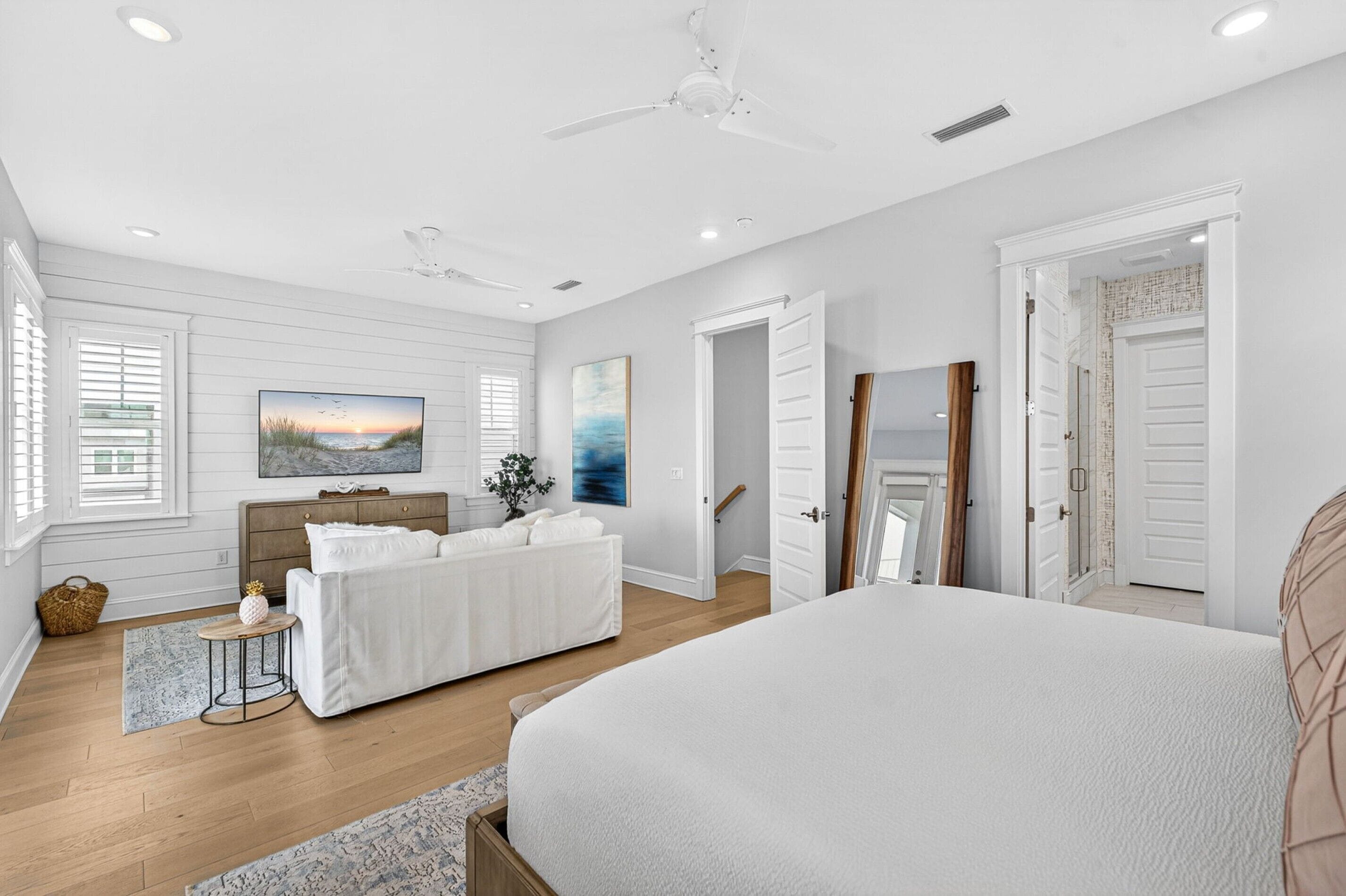 A bedroom with a large bed, a nightstand, a dresser, a ceiling fan, and a painting on the wall.