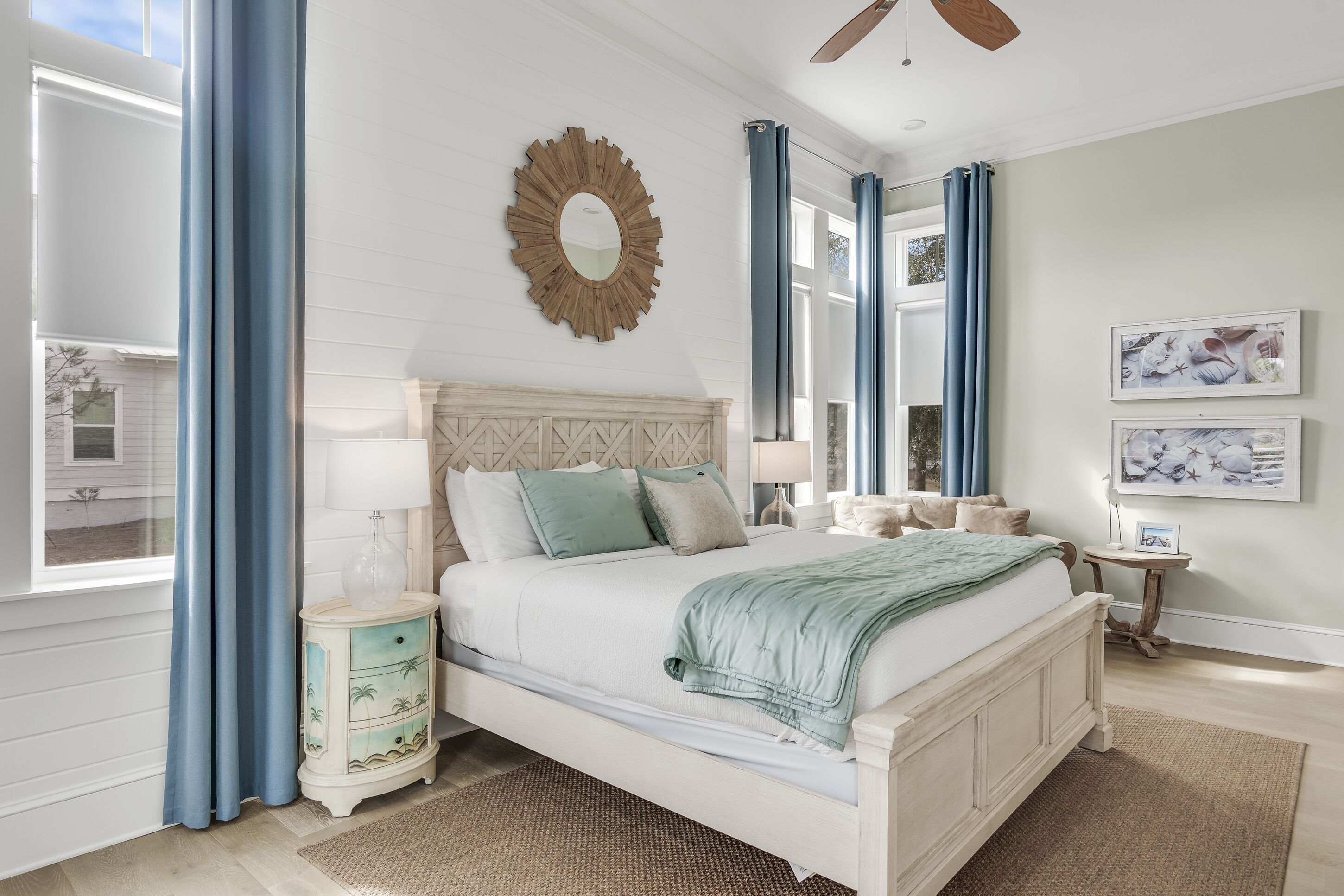 A bedroom with a bed, a nightstand, a mirror, and a window with curtains.