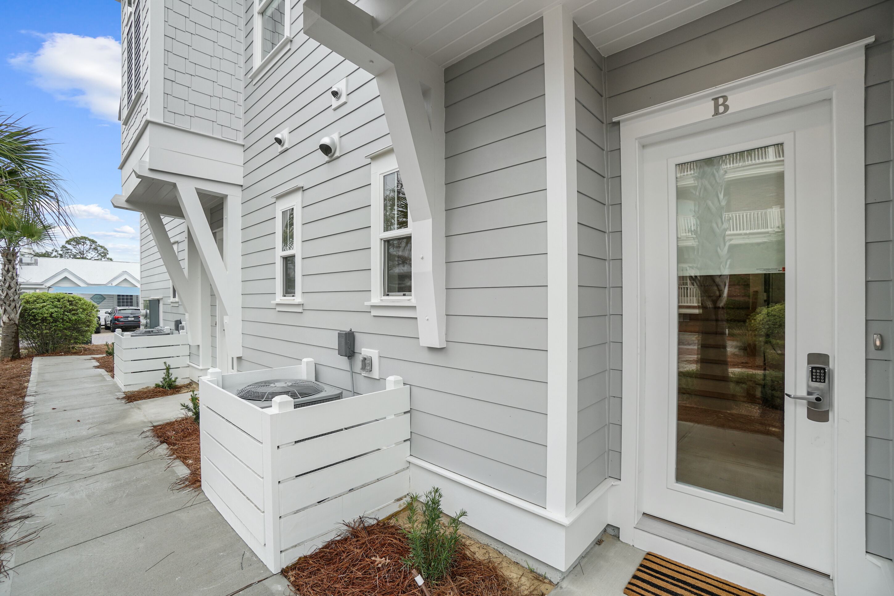 A white two-story house with a front door marked 'B', a small porch, and a concrete pathway.