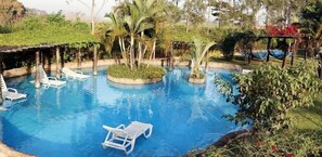 A pool with white lounge chairs, surrounded by greenery and a pergola. - Mirante Praia Hotel (Olímpia)