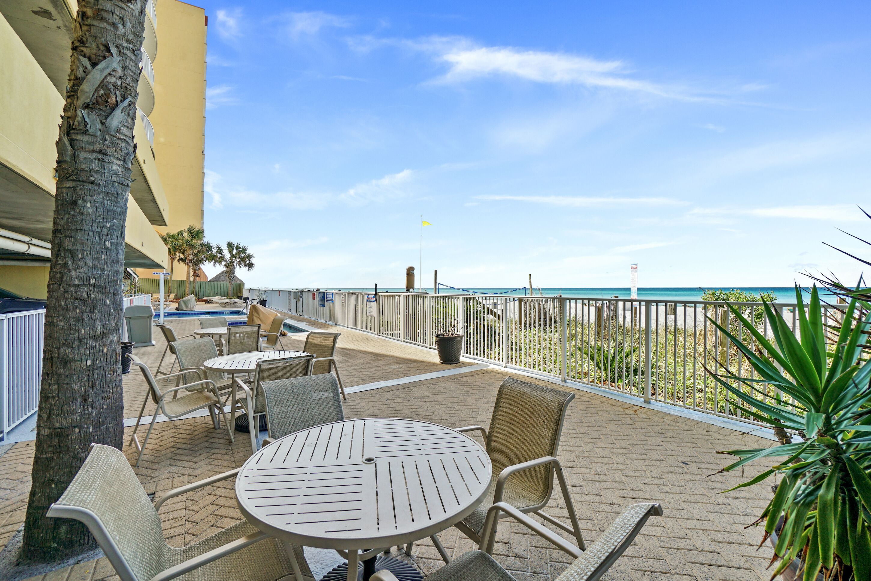 An outdoor patio with tables and chairs, a pool, and a view of the beach.