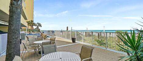 An outdoor patio with tables and chairs, a pool, and a view of the beach.