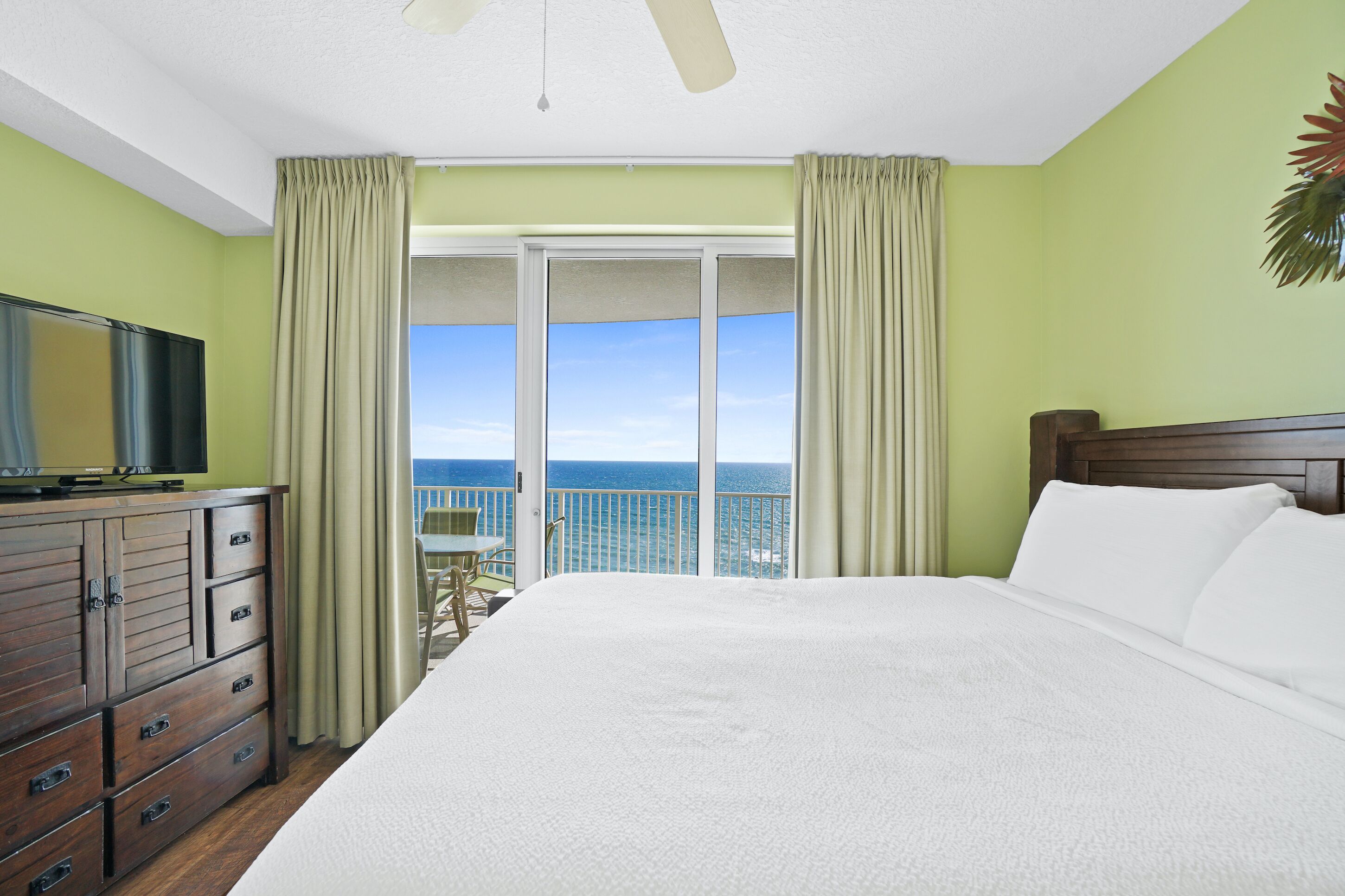 Een hotelkamer met een groot bed, een televisie op een houten dressoir en een balkon met uitzicht op de oceaan.