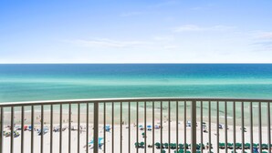 A beach with clear turquoise water, a balcony railing, and beach umbrellas. - Emerald Isle Beach Resort by Panhandle Getaways (Panama City Beach)