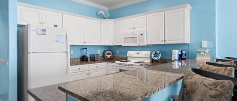 Cocina con gabinetes blancos, encimera de granito y microondas.